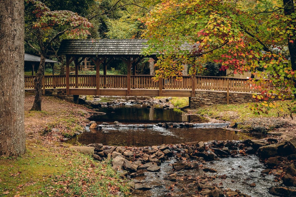 Uma ponte de madeira sobre um riacho, com um coreto ao fundo.