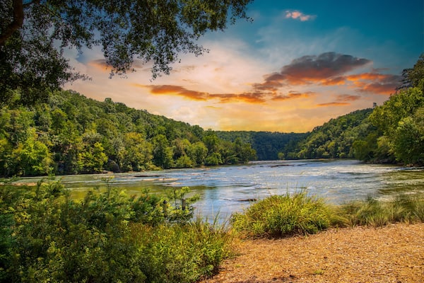 a gorgeous summer landscape along the Chattahoochee river with flowing river water surrounded by lush green trees, grass and plants with powerful clouds at sunset at Walton On The Chattahoochee