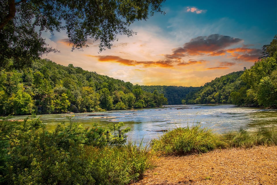 A river flowing through a forested valley with dense greenery and a clear sky.
