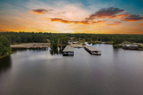 an aerial shot of the vast still waters of Lake Tobesofkee with homes and docked boats in the marina surrounded by vast miles of lush green trees and grass with powerful clouds at sunset in Perry