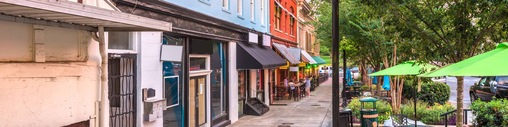 Una calle colorida bordeada de edificios, mesas al aire libre y árboles.