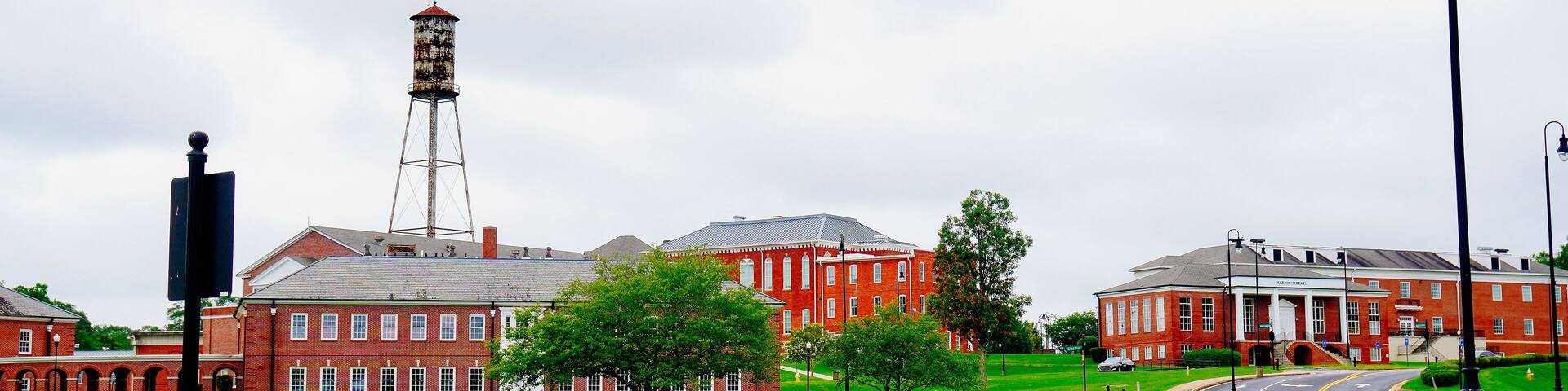 A red brick building with a water tower, a green lawn, and a road with a traffic light.
