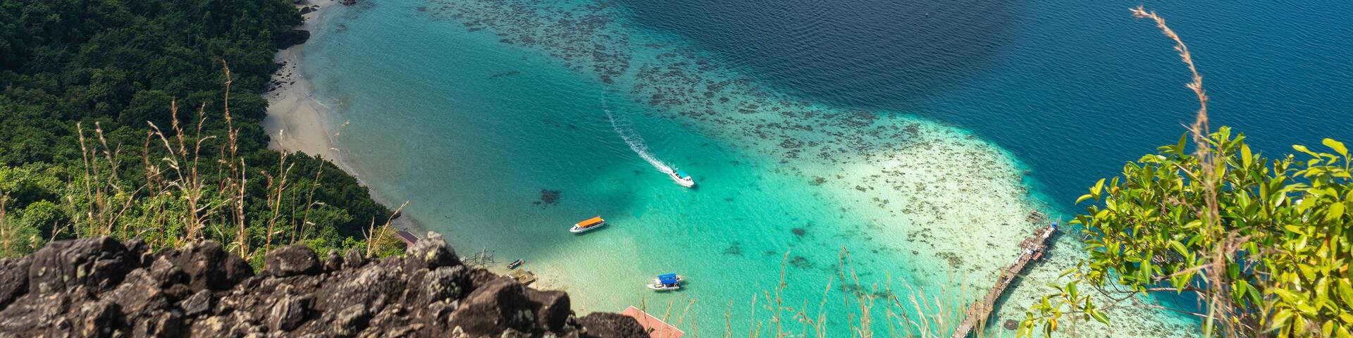 Spectacular view from above showcasing vibrant turquoise waters meeting a lush green coastline, dotted with boats, under a clear blue sky.