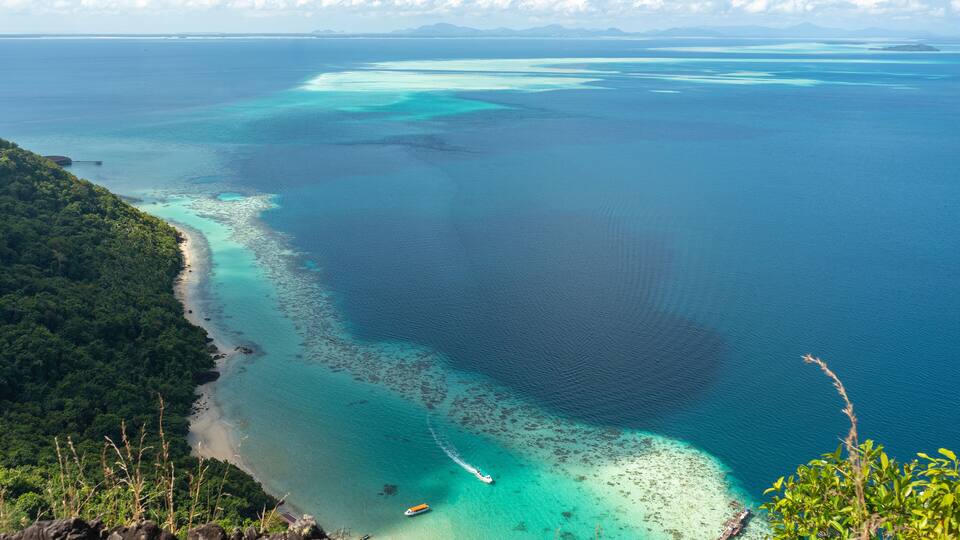 Spectacular view from above showcasing vibrant turquoise waters meeting a lush green coastline, dotted with boats, under a clear blue sky.
