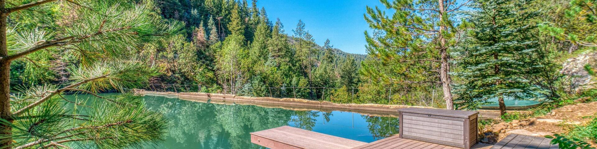 A wooden deck overlooking a calm lake surrounded by pine trees.