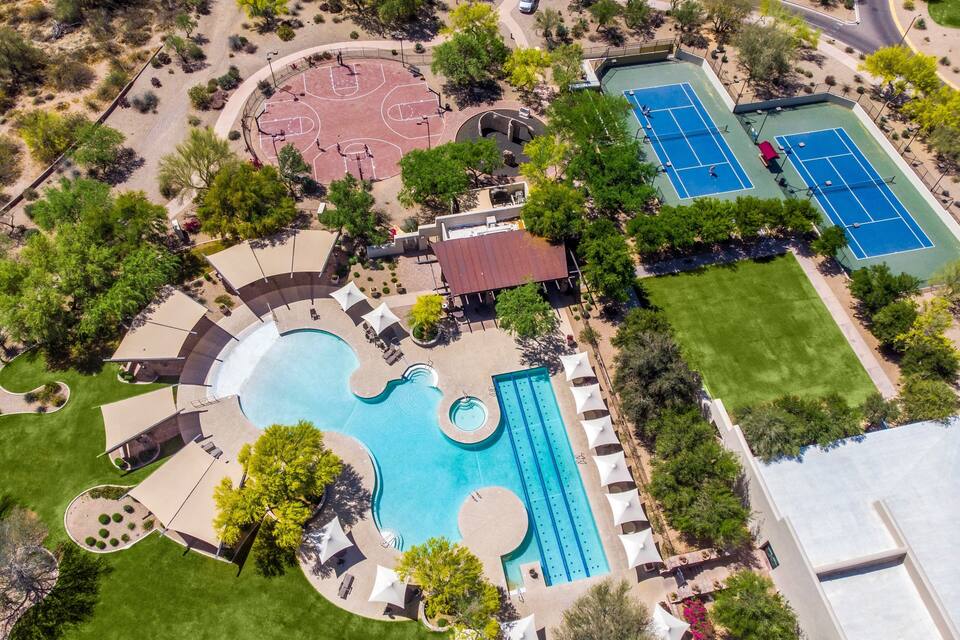 An aerial view of a residential area with a swimming pool, tennis courts, and a basketball court.