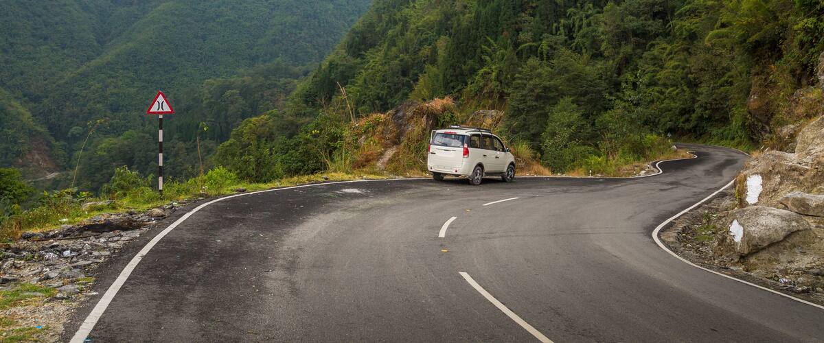 A winding mountain road with a van, surrounded by lush greenery and rocky terrain.