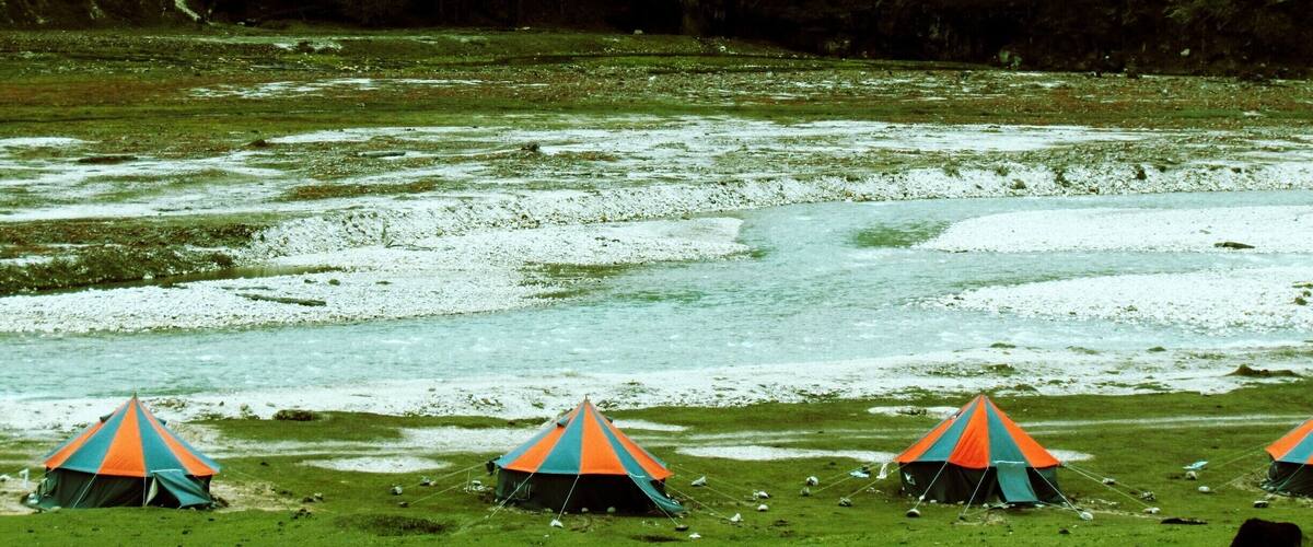 A grassy field with tents and a river.