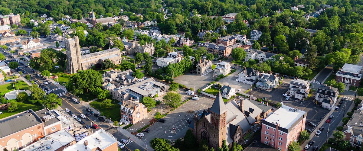 An aerial view of a town with historic buildings, a prominent church, and surrounding green hills.