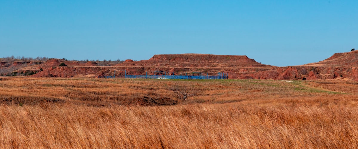 A landscape with rolling hills, dry grass, and a blue fence.