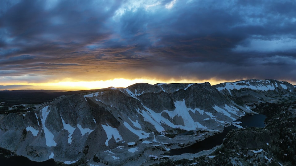 A mountain range with snow patches and a winding road.