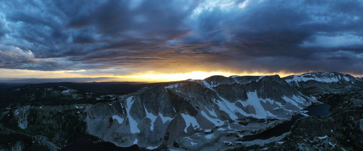 A mountain range with snow patches and a winding road.