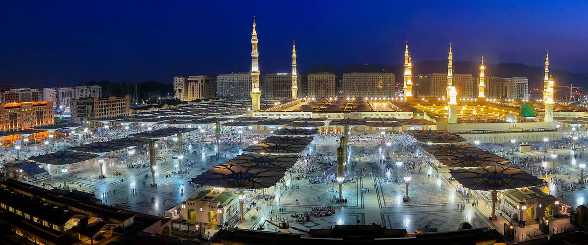A large, illuminated mosque complex with multiple minarets and a central dome.