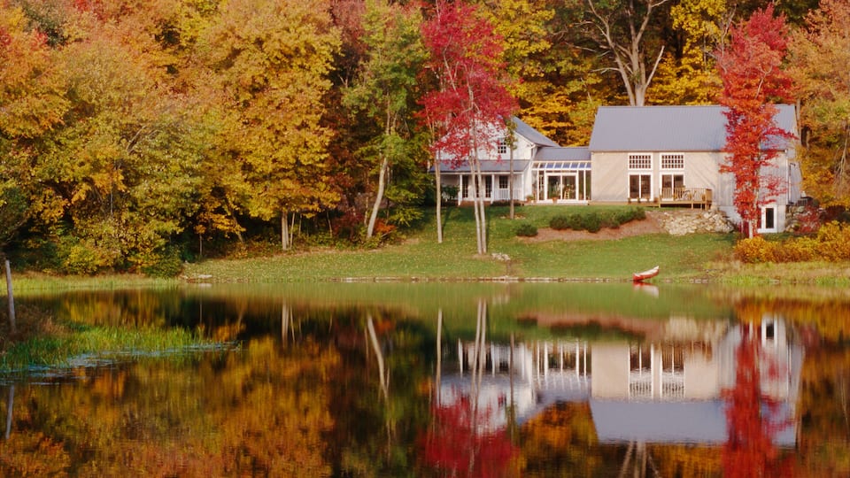 A house surrounded by autumn-colored trees and a calm lake.