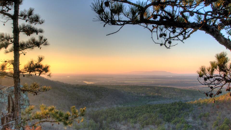 A forested landscape with a clear view of distant mountains during sunset.