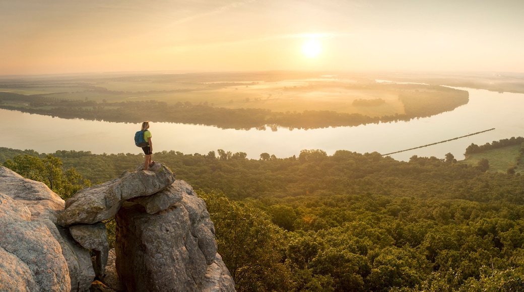 Woman standing on sandstone overhang watching sunrise from summit of Petit Jean Mountain above Arkansas River ValleyÂ