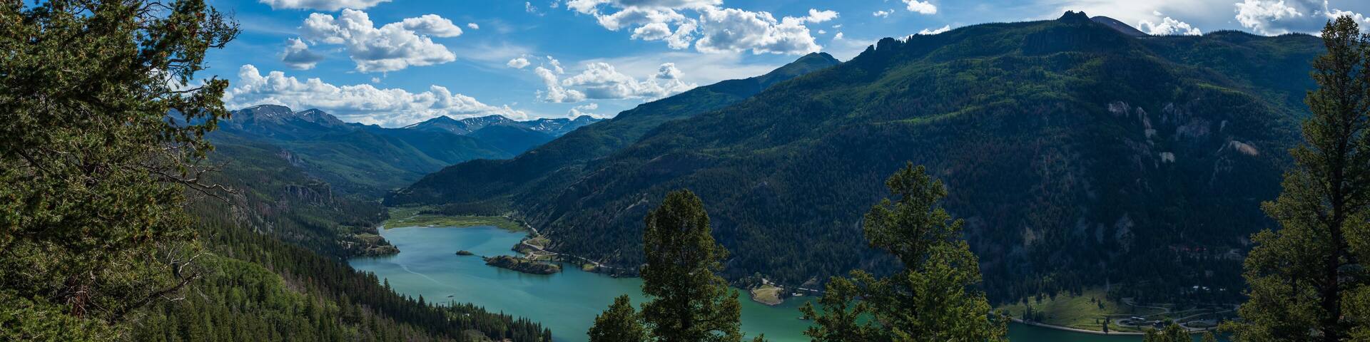 A mountainous landscape with a lake surrounded by dense forests and a clear sky.