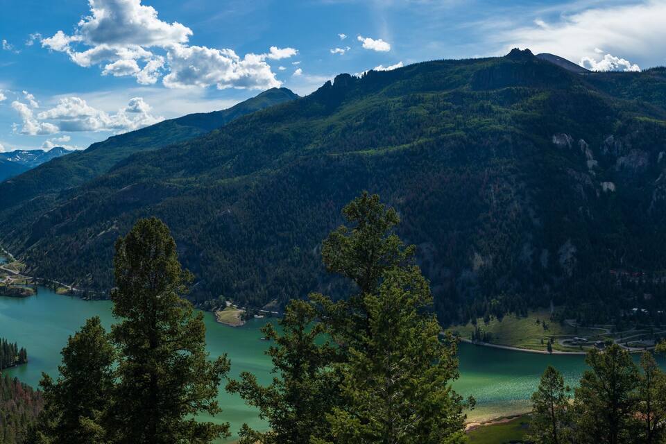 Un paysage montagneux avec un lac entouré de forêts denses et un ciel dégagé.