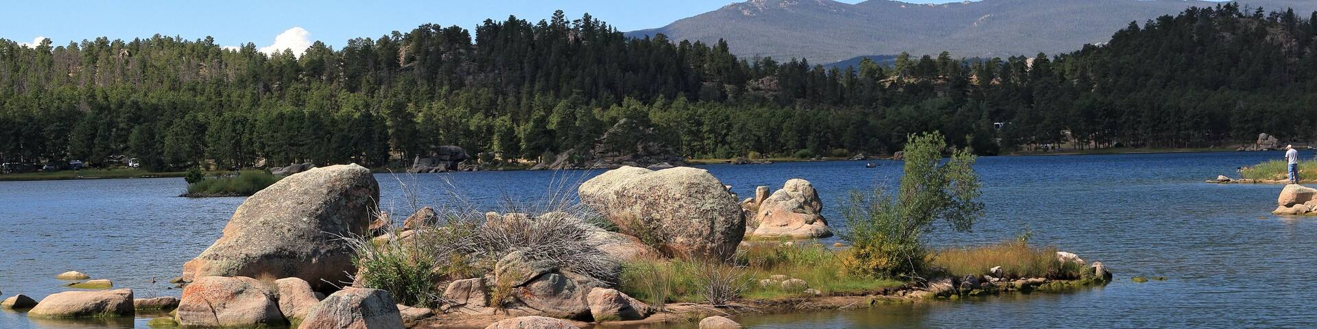 Un lago rodeado de rocas grandes y árboles, con montañas al fondo.