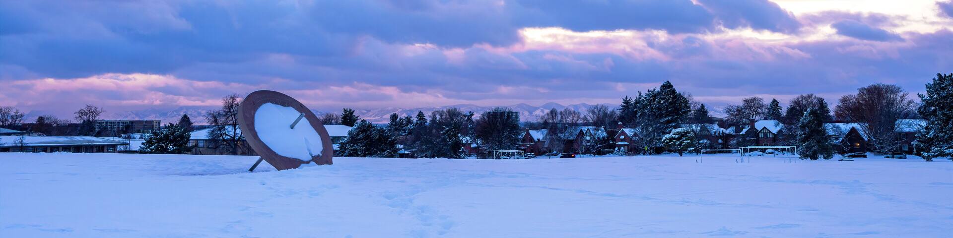 A snowy landscape with a satellite dish in the foreground and houses in the background under a colorful sky.