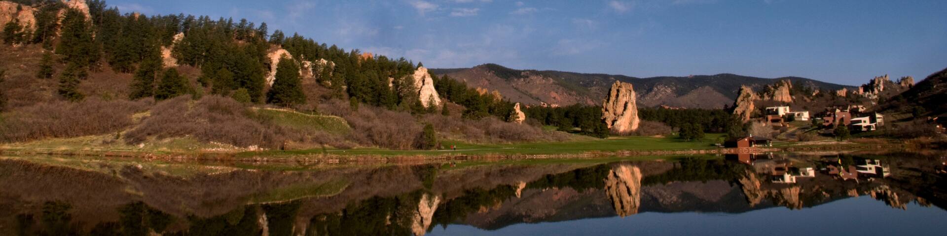 A calm lake reflecting the sky and surrounding landscape, with a village nestled among hills and trees.