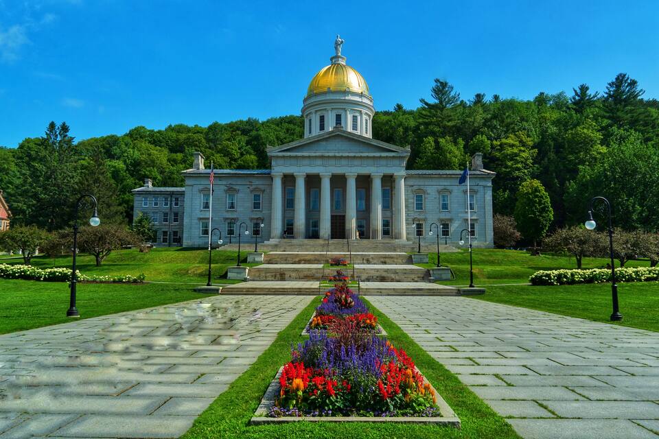 A large building with a golden dome, surrounded by a well-maintained garden and a paved walkway.