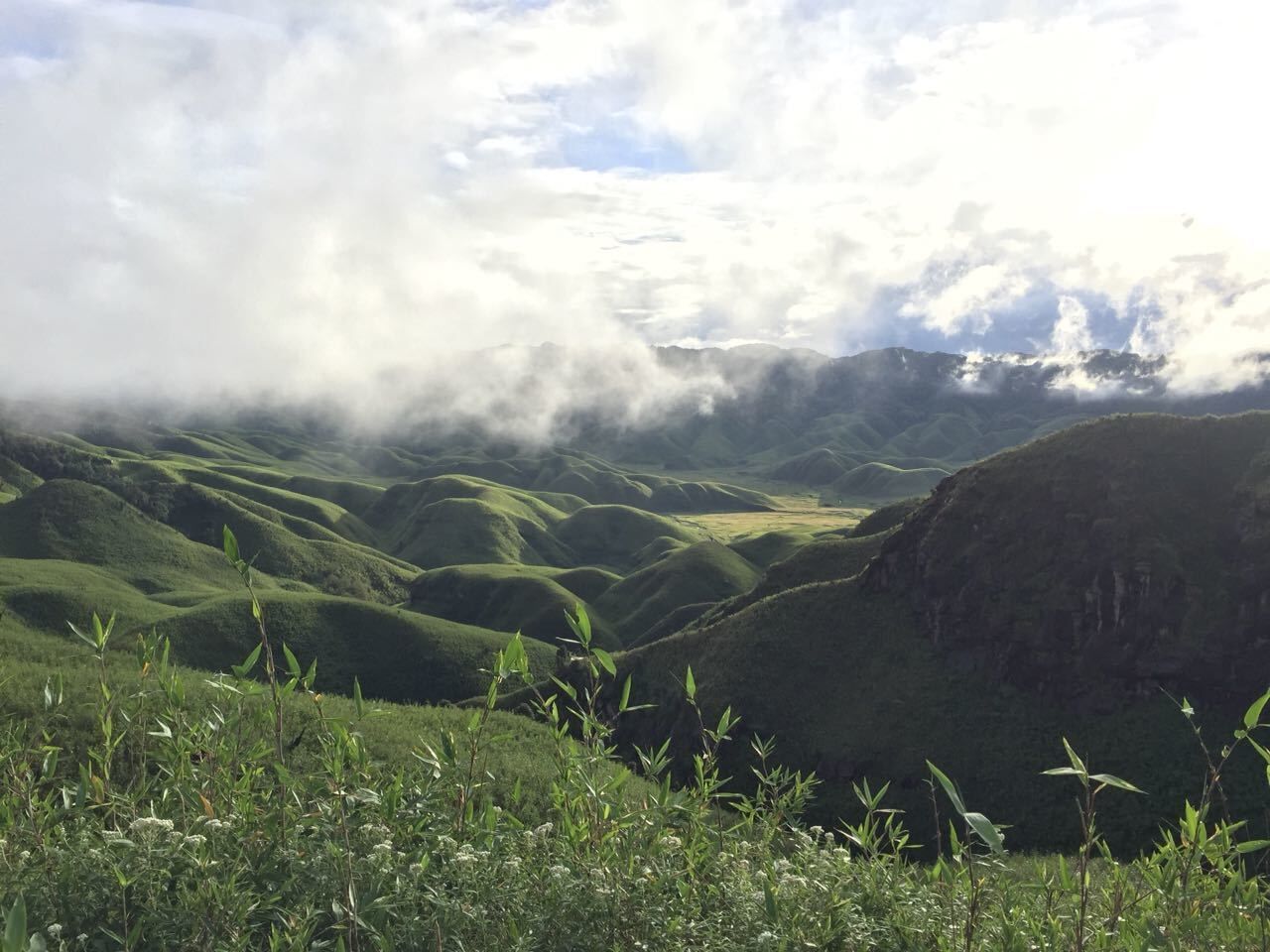 Rolling green hills, a valley, and a mountain range with clouds above.