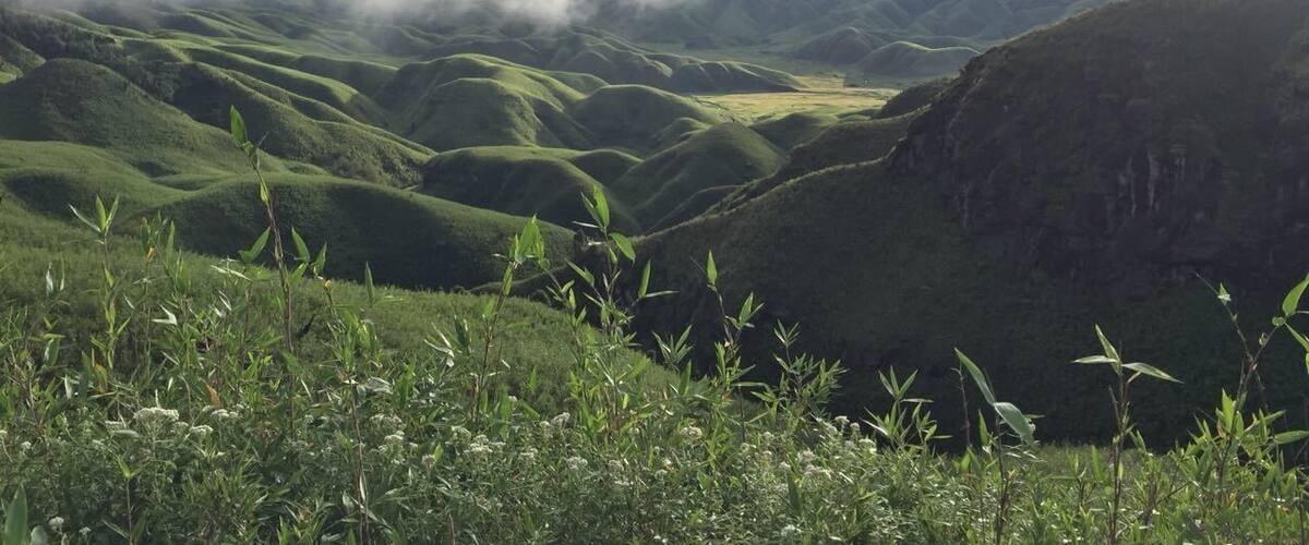 Rolling green hills, a valley, and a mountain range with clouds above.