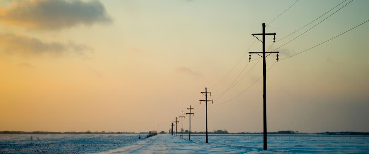 A snow-covered road with utility poles and power lines extending into the distance.