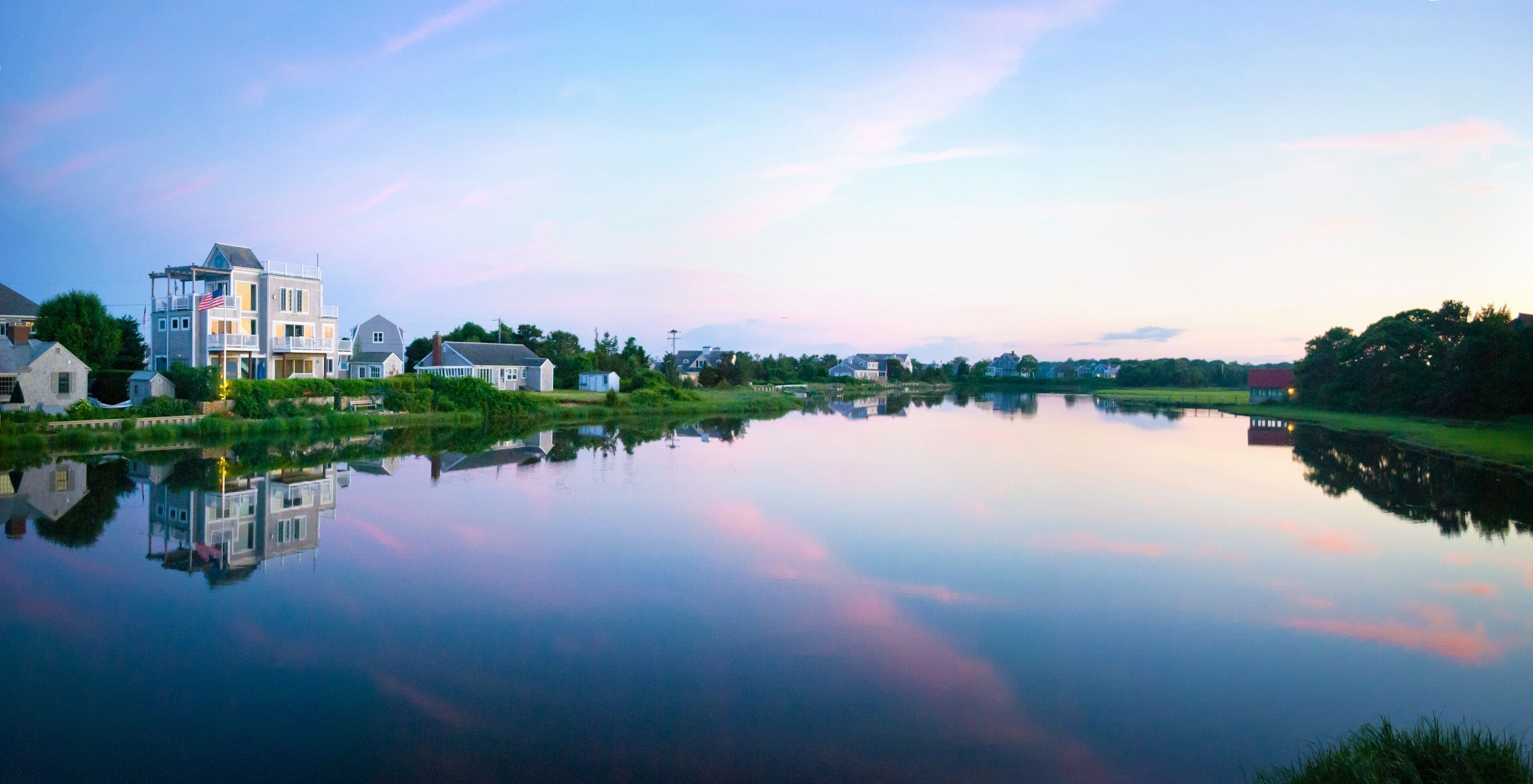 A calm river reflecting houses and a clear sky.