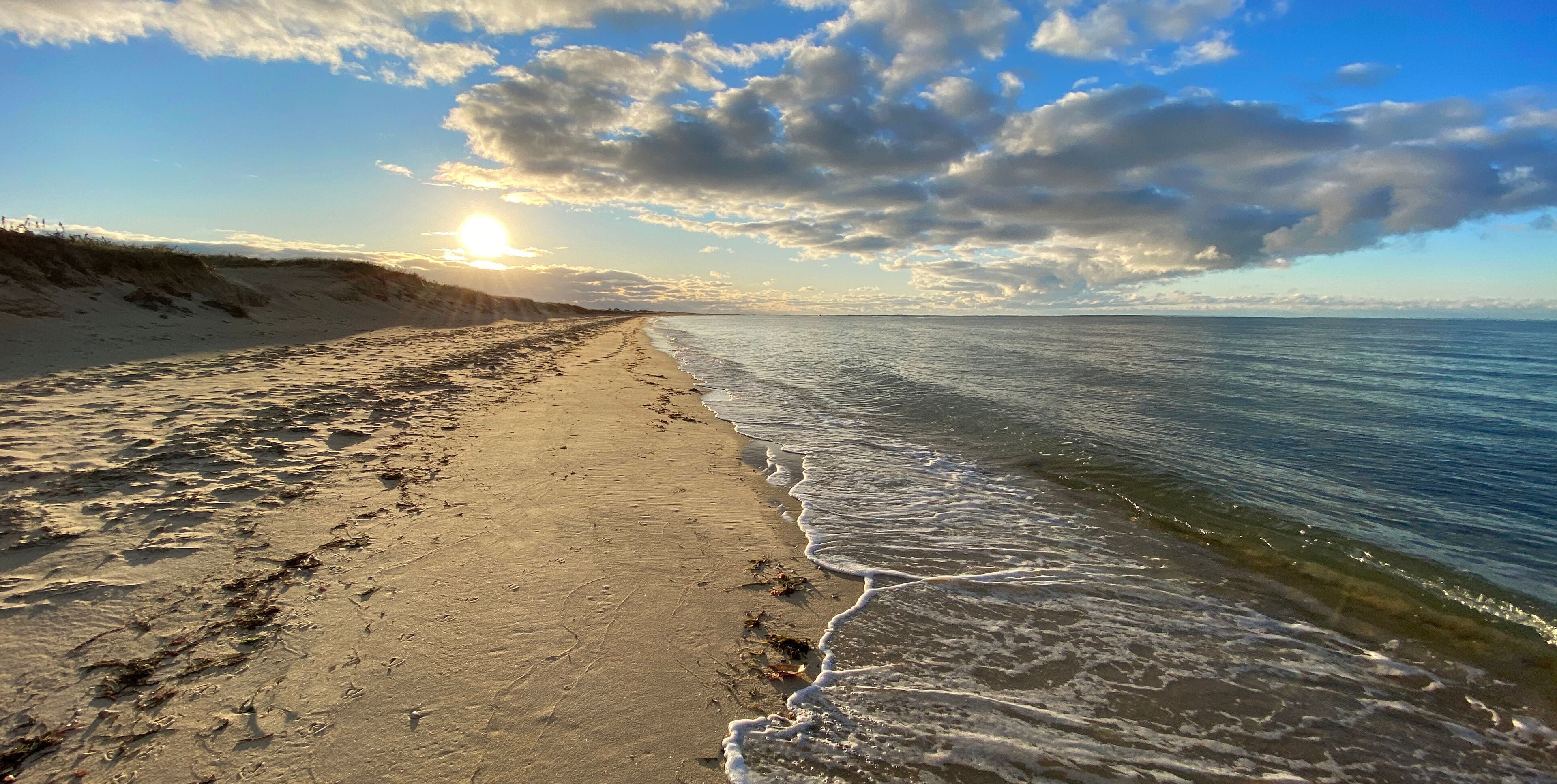 A beach with sand, waves, and a cloudy sky.