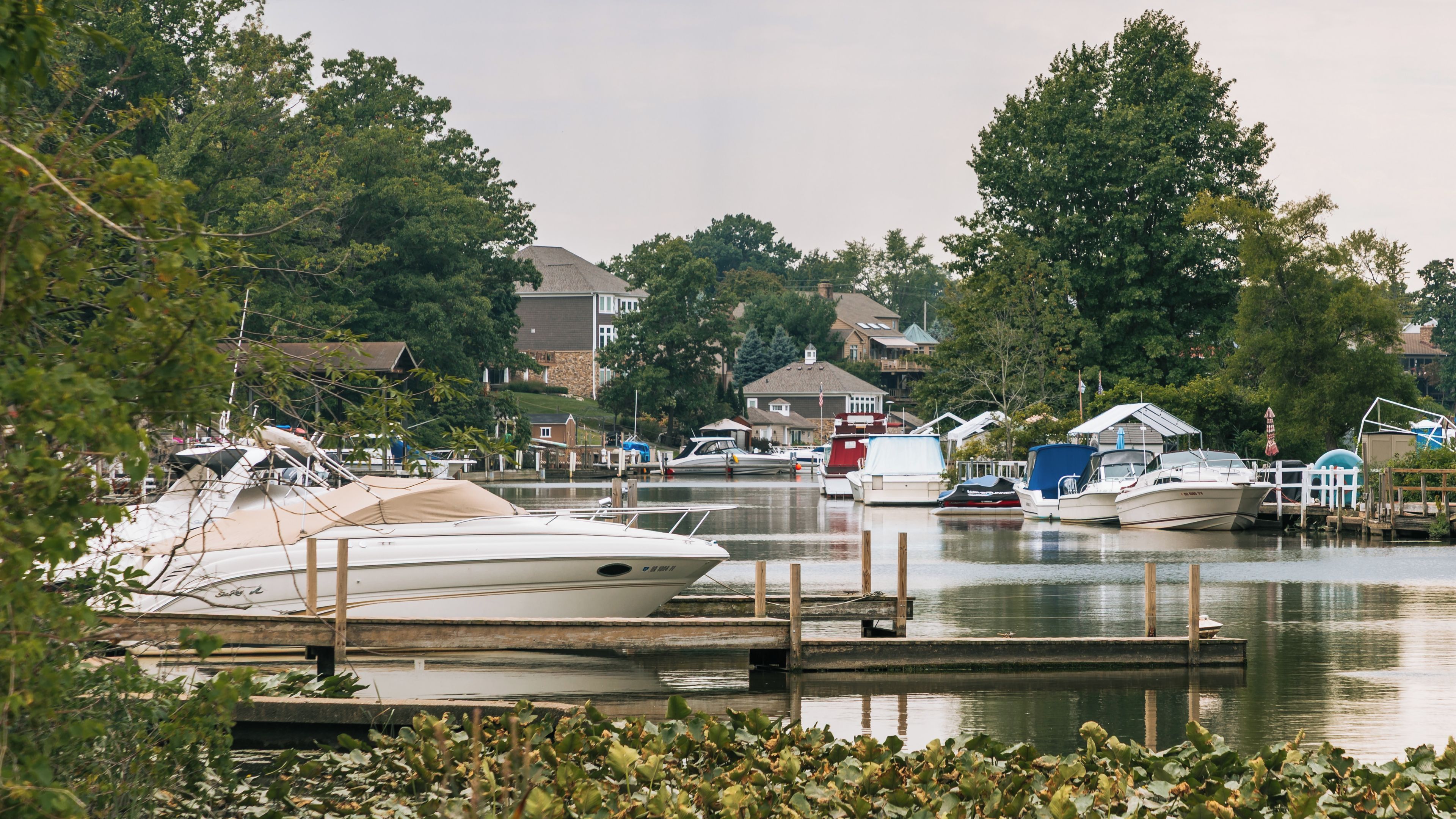 A marina with boats docked, surrounded by trees and houses.