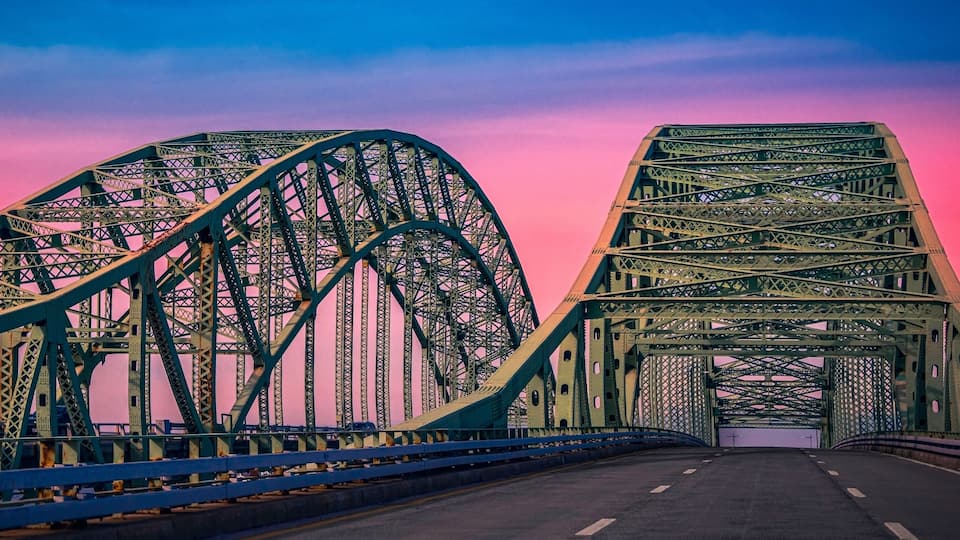 A steel bridge with a pink sky in the background.
