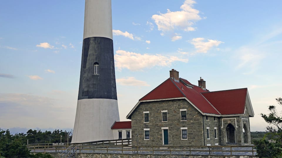 A lighthouse with a red roof and a stone building beside it.