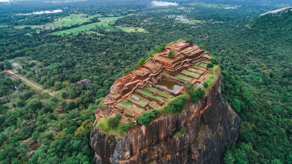 An ancient stone structure perched on a cliff, surrounded by dense forest.