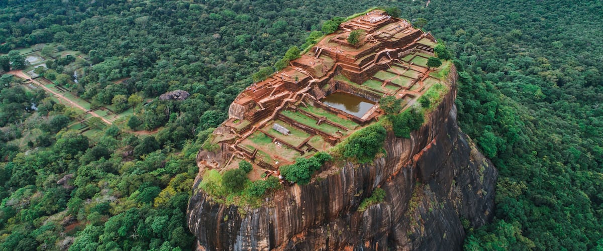 An ancient stone structure perched on a cliff, surrounded by dense forest.