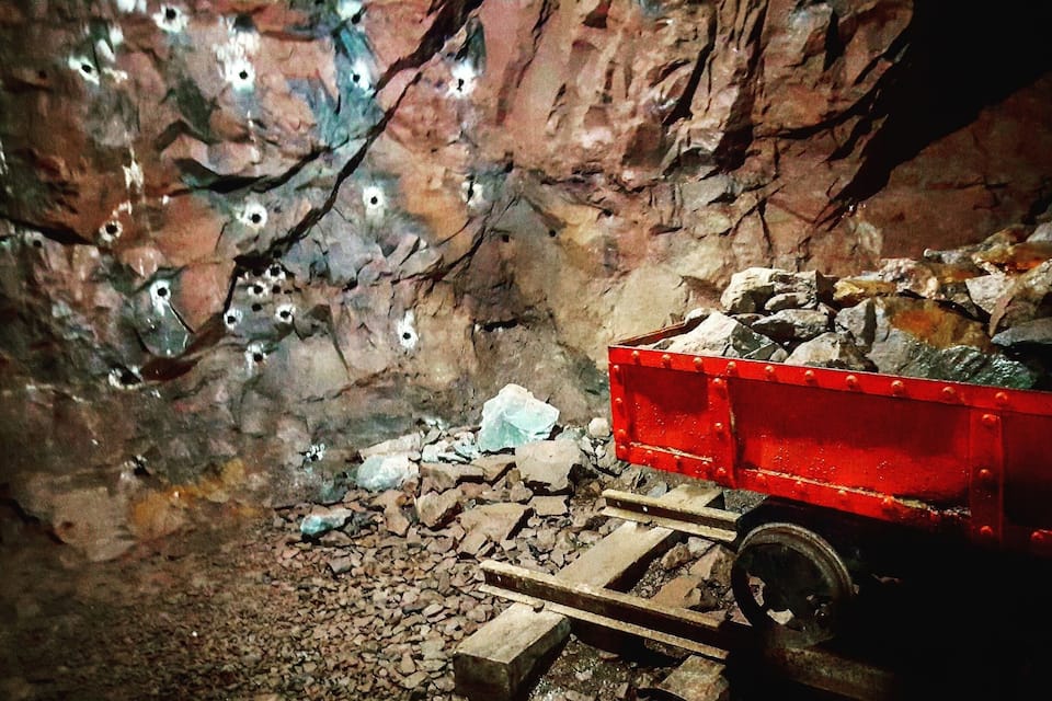 Un vagó de mineria en un túnel rocós amb forats visibles a les parets.