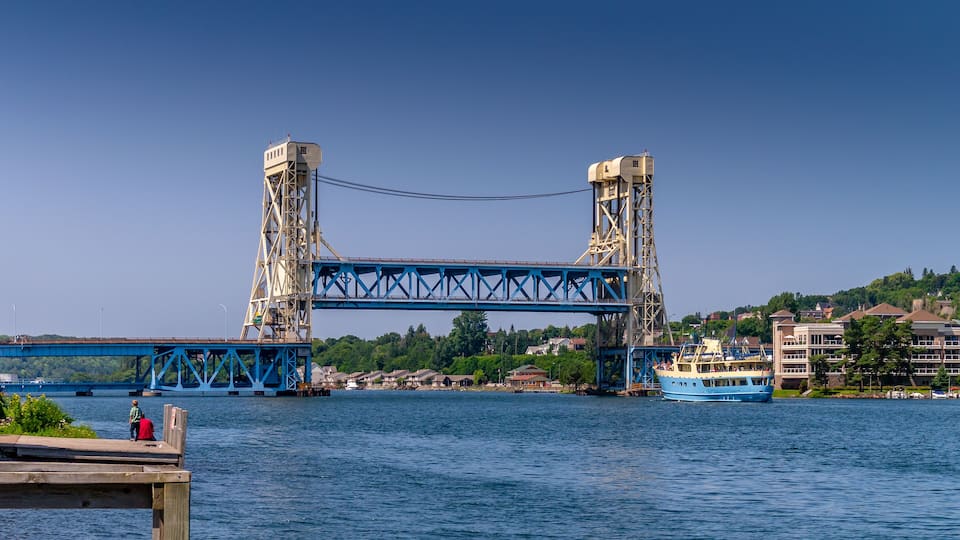 A large blue bridge spanning a river with a boat docked nearby.