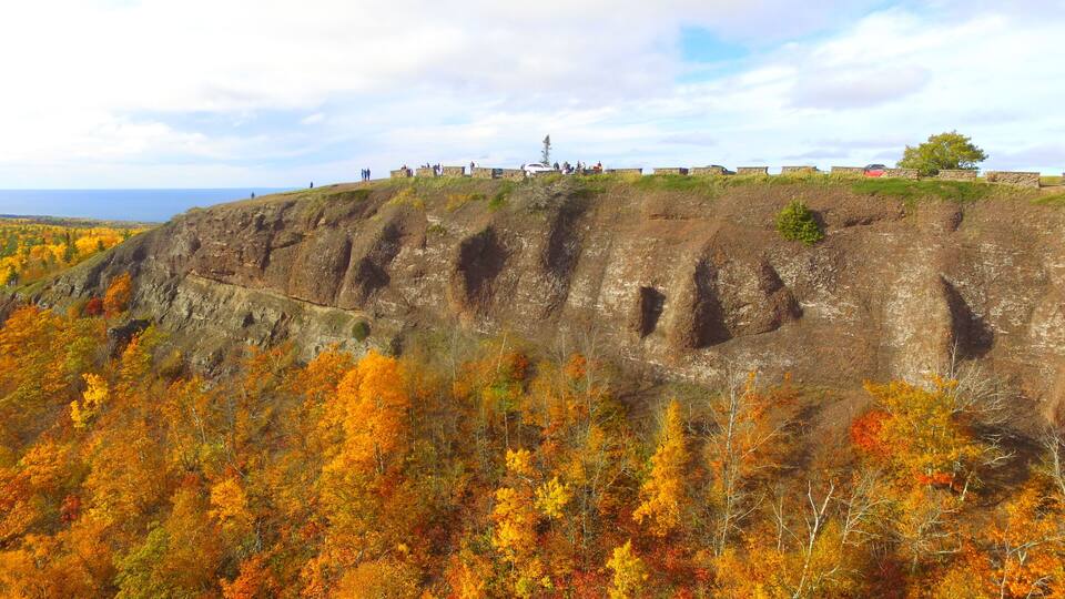 A rocky cliff with autumn foliage and a stone wall with people on top.