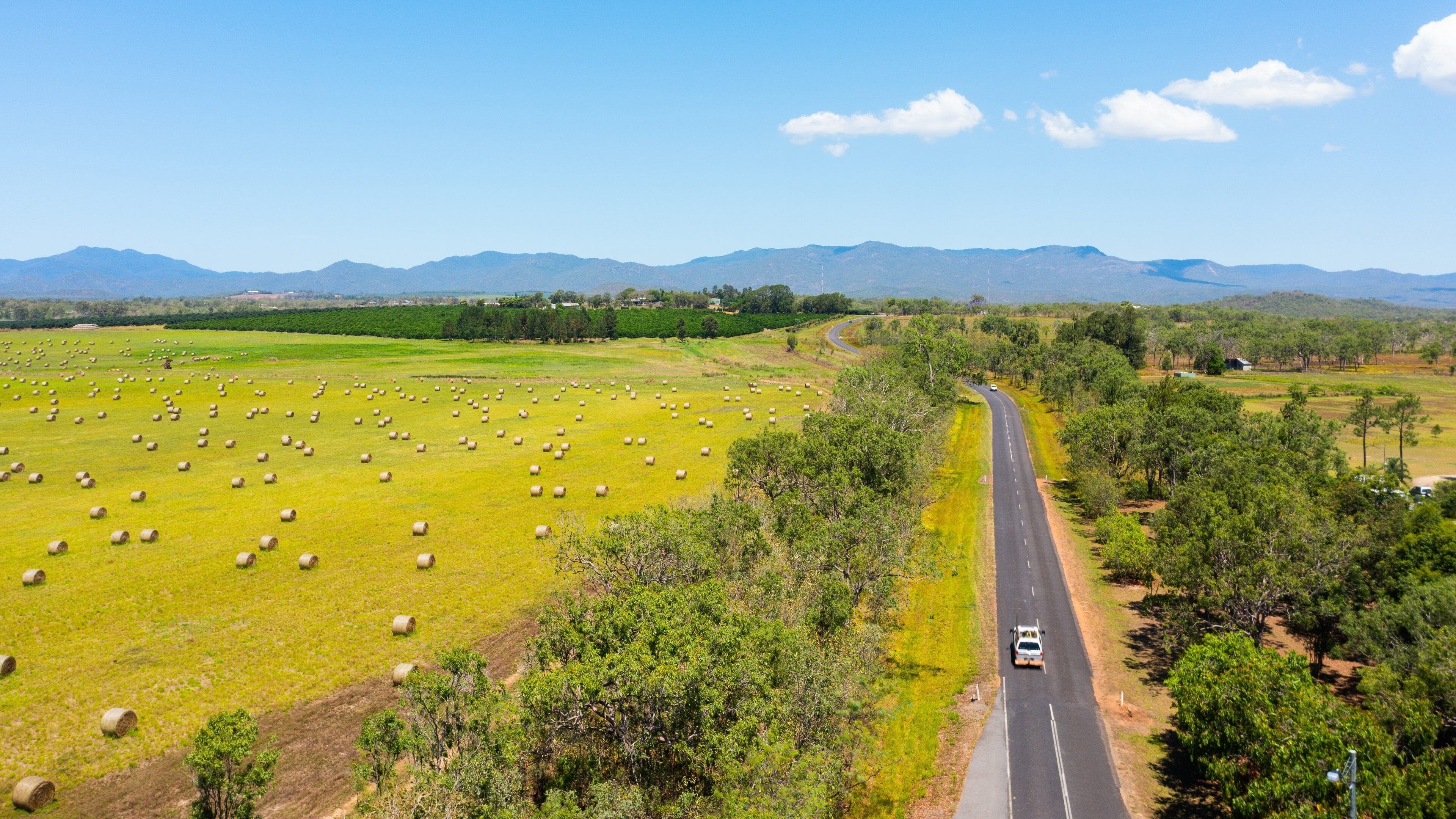 A rural landscape with a road, hay bales, and distant mountains.