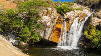 Una cascada que se precipita sobre rocas rodeadas de exuberante vegetación.