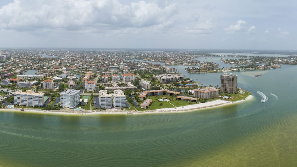 A coastal cityscape with high-rise buildings, a marina, and a bay with clear waters.