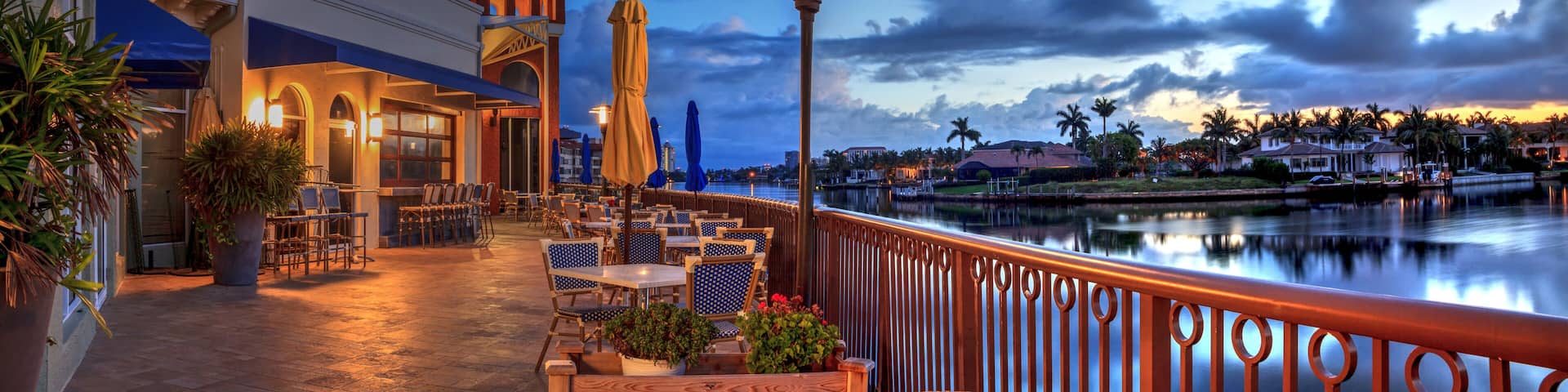 A waterfront patio with outdoor seating, a lamp post, and a view of the water and distant buildings.