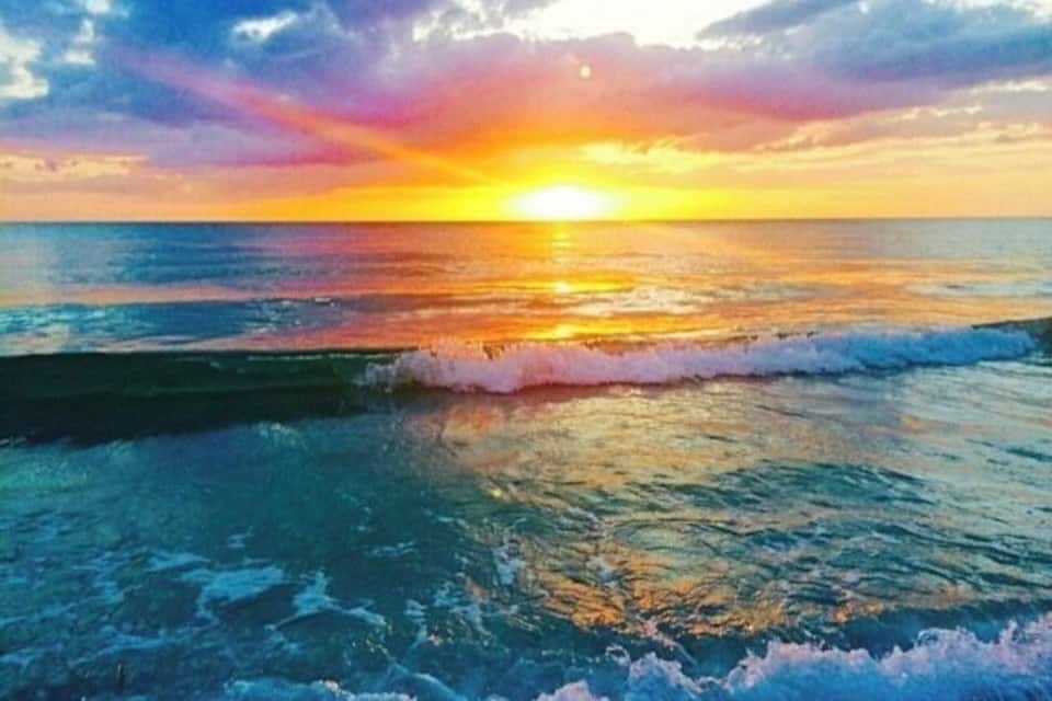 Ein Sonnenuntergang über dem Meer mit Wellen und einem farbenprächtigen Himmel.