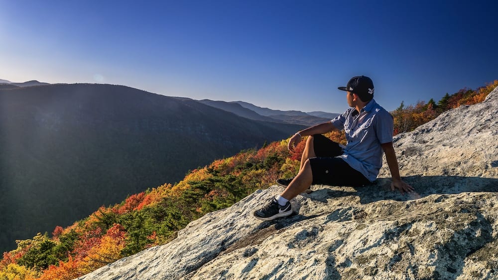 A person sitting on a rock with a mountainous landscape in the background.