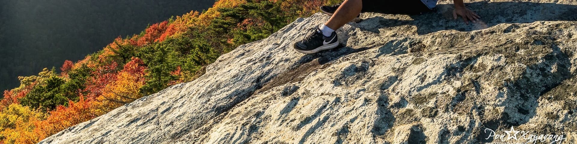 A person sitting on a rock with a mountainous landscape in the background.