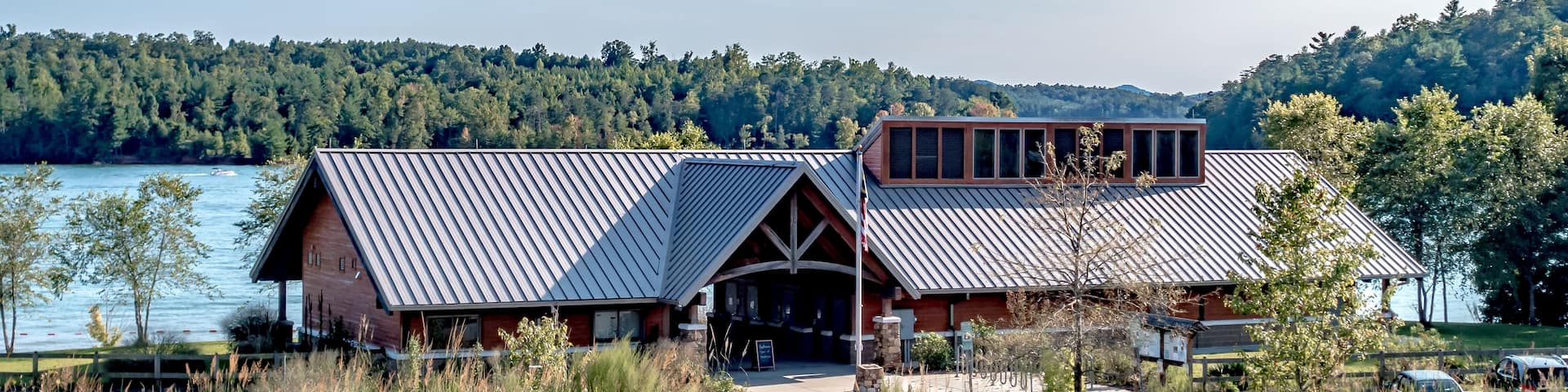 A lodge with a metal roof, a wooden deck, and a view of a lake and forest.