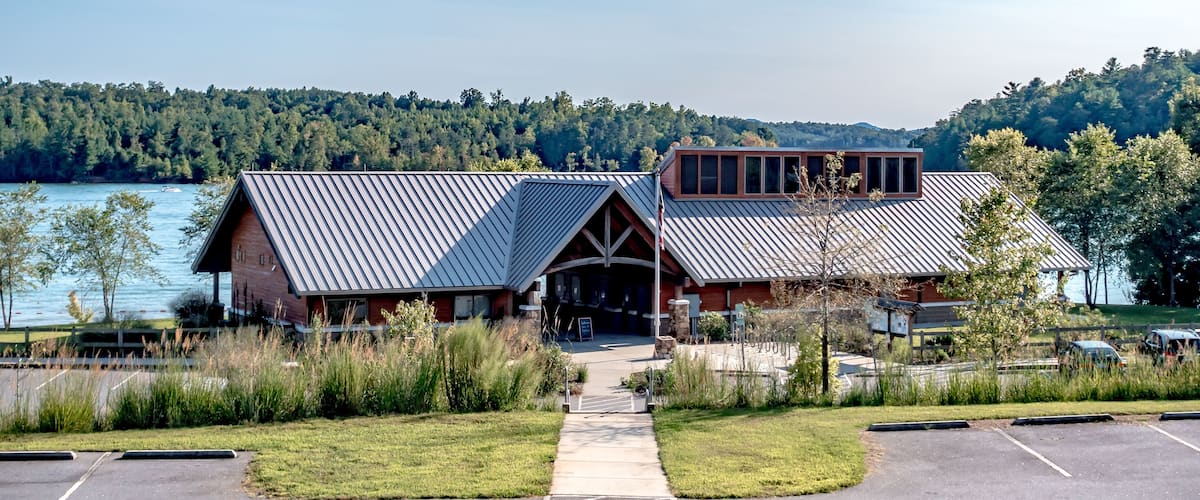 A lodge with a metal roof, a wooden deck, and a view of a lake and forest.