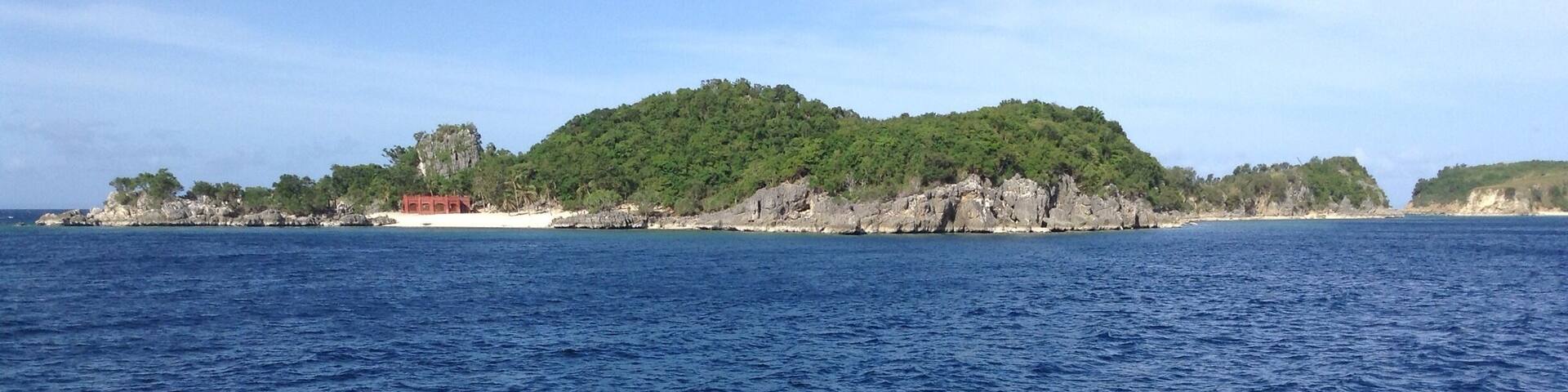 A coastal landscape with a rocky island covered in greenery and a clear blue sea.