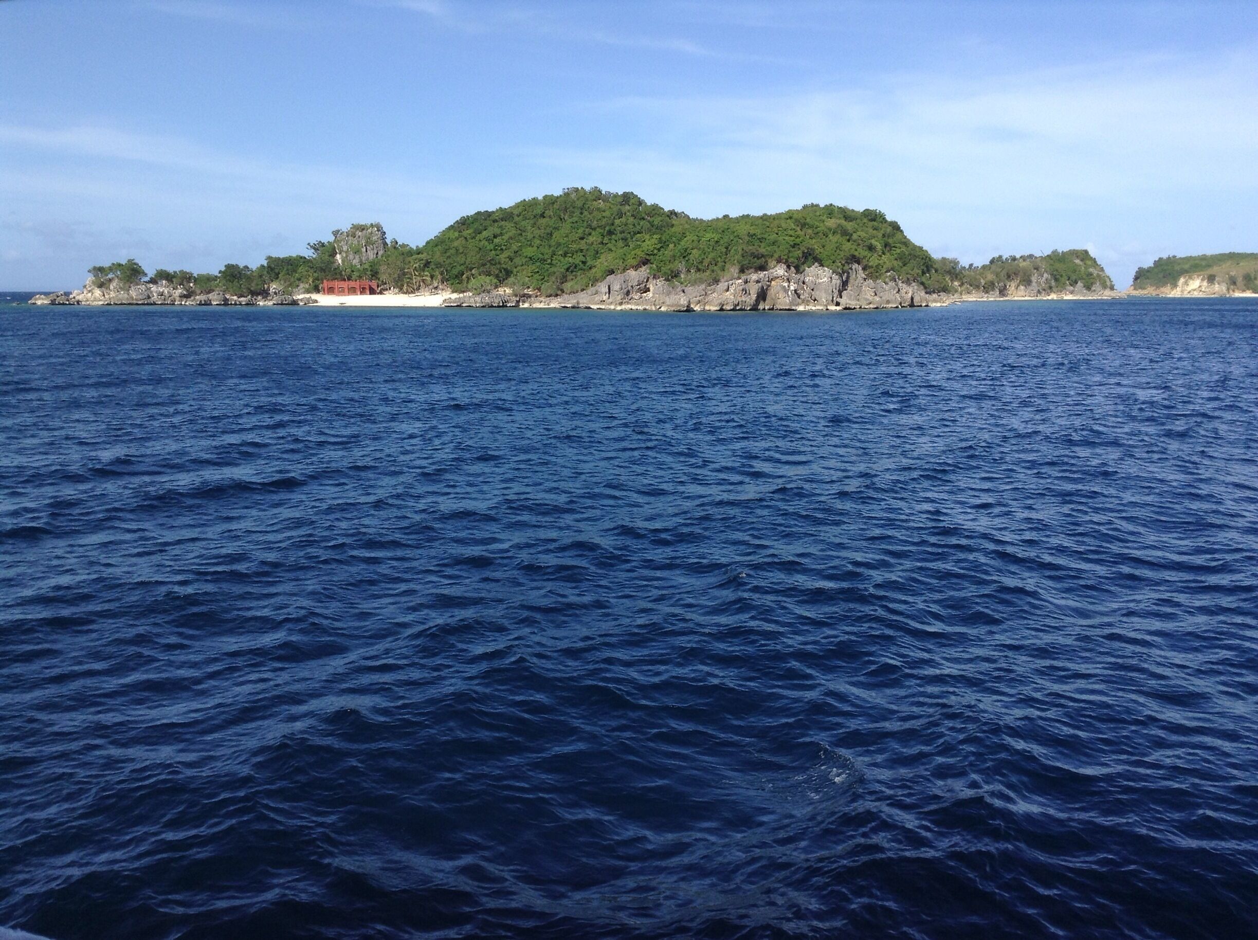 A coastal landscape with a rocky island covered in greenery and a clear blue sea.